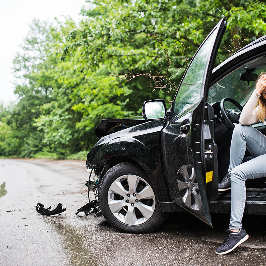 Young frustrated woman sitting in the damaged car after a car accident, making a phone call.